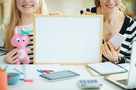Closeup on happy modern mother and child in striped sweaters in home office in the modern house in sunny day showing blank billboard.の写真素材