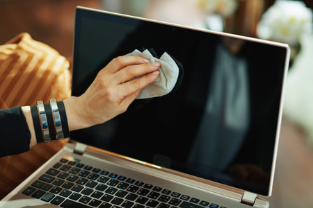 Closeup on woman wiping laptop display with cleaning cloth in the living room in sunny day.