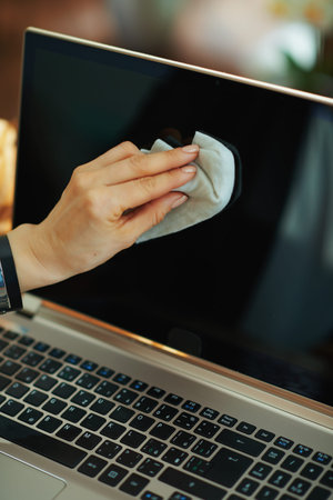 Closeup on woman cleaning laptop display with cleaning cloth at home in sunny day.
