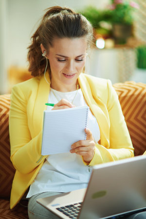 smiling modern student in jeans and yellow jacket in the modern house in sunny day watching internet lessons on a laptop.の写真素材