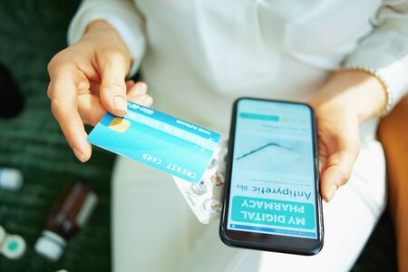 Upper view of woman with credit card and empty blister pack of pills buying pharmacy online using smartphone at home in sunny day.の写真素材