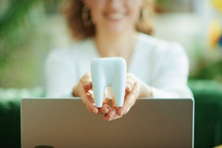 Closeup on smiling woman with laptop showing tooth in the living room in sunny day.の写真素材