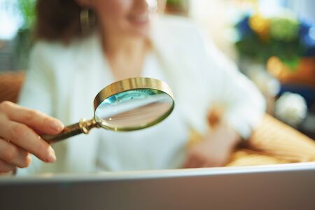 Closeup on woman with laptop using magnifying glass in the living room in sunny day.の写真素材