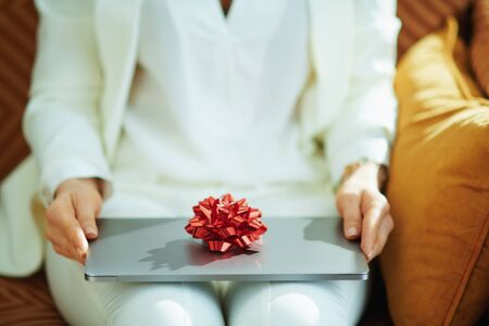 Closeup on woman in white blouse and jacket and gift laptop with red bow at home in sunny day.の写真素材