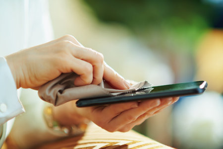 Closeup on female cleaning smartphone with cleaning cloth at home in sunny day.の写真素材