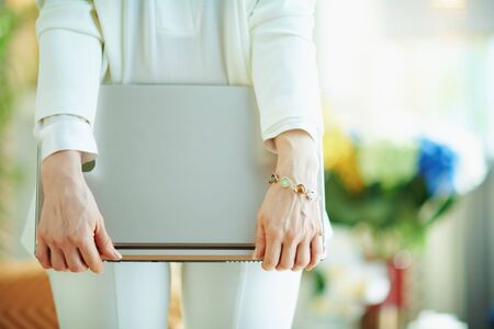 Closeup on happy woman in white blouse and jacket in the living room in sunny day holding closed laptop.の写真素材