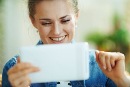 smiling stylish 40 years old woman in jeans shirt with tablet PC study online in the modern living room in sunny day.の写真素材