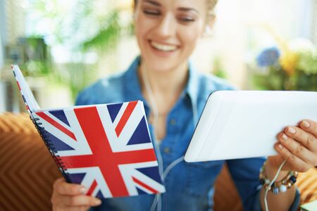 Closeup on smiling woman with tablet PC and UK flag notebook learning foreign language online in the living room in sunny day.の写真素材