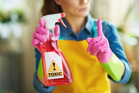 Closeup on woman in orange apron and pink rubber gloves with raised finger and spray bottle of cleaning toxic supplies in the living room in sunny day. toxic cleaning supplies conceptの写真素材