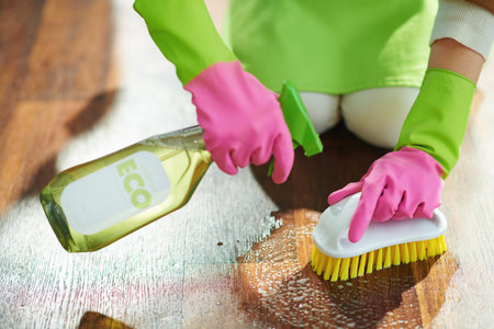 Closeup on woman in green apron and pink rubber gloves with spray bottle of eco friendly cleaning...