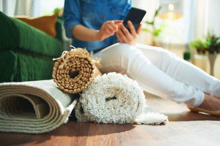 Closeup on woman in jeans shirt and white pants with pile of carpets searching for carpet cleaning...