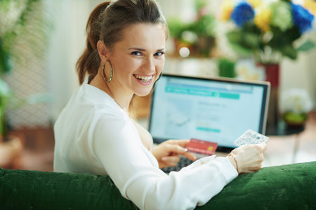 Portrait of happy modern 40 years old woman in white blouse with credit card and empty blister pack...