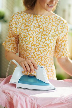 Closeup on woman in yellow dress at home in sunny day ironing on ironing board.の写真素材