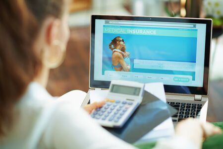 Seen from behind woman at home in sunny day choosing medical insurance digitally on a laptop.の写真素材
