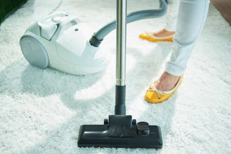 Closeup on woman in the living room in sunny day vacuuming white fluffy carpet.の写真素材