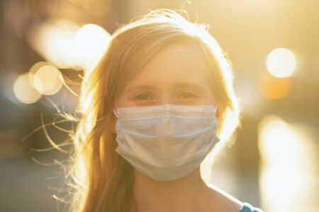 Life during coronavirus pandemic. Portrait of modern girl in blue overall with medical mask outdoors in the city.の写真素材