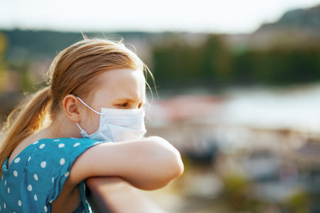 Life during coronavirus pandemic. modern child in blue overall with medical mask looking into the distance outdoors in the city.の写真素材