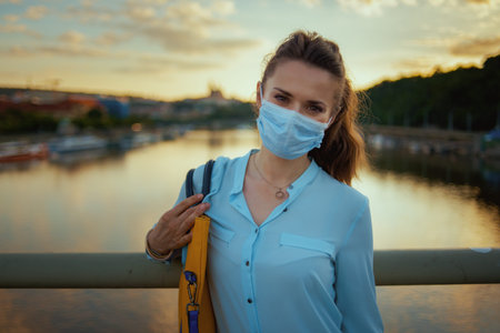 Life during covid-19 pandemic. Portrait of young woman in blue blouse with medical mask and handbag...