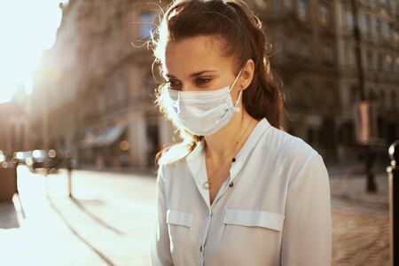 Life during covid-19 pandemic. Portrait of pensive young woman in blue blouse with medical mask outdoors on the city street.の写真素材