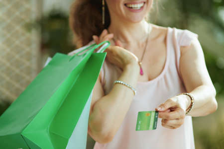 Portrait of happy trendy 40 years old woman shopper in pink blouse with credit card and paper shopping bags.の写真素材