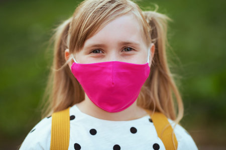 Life during covid-19 pandemic. girl in white polka dot blouse with yellow backpack going from school...