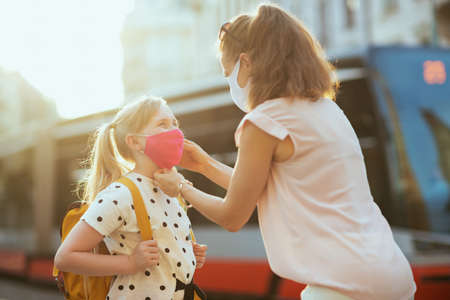 Portrait of elegant mother and child with masks and yellow backpack getting ready for school outside.の写真素材
