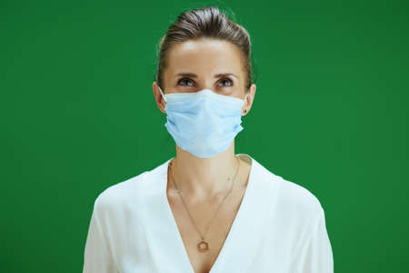 Portrait of modern woman pedagogue in white blouse with medical mask against chalkboard green background.の写真素材
