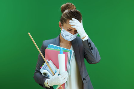 stressed modern 40 years old woman teacher in white blouse with medical mask, rubber gloves, digital thermometer, textbook and sanitizer isolated on chalkboard green background.の写真素材