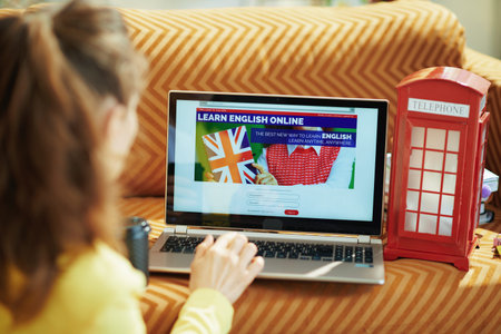 Portrait of happy young woman in yellow jacket with headphones showing learning foreign language online site on a tablet PC in the modern house in sunny day.の写真素材
