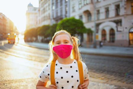 Life during covid-19 pandemic. Seen from behind girl in white polka dot blouse with yellow backpack going from school outside.の写真素材
