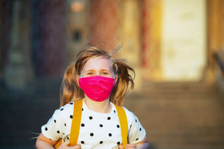 Life during covid-19 pandemic. Seen from behind girl in white polka dot blouse with yellow backpack going from school outside.の写真素材