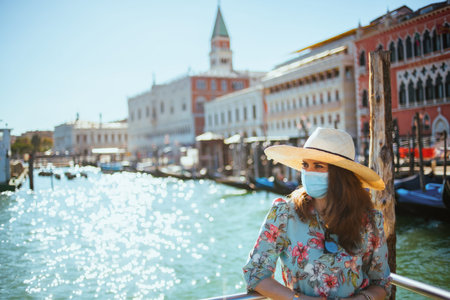 Travel during coronavirus pandemic. Seen from behind modern solo tourist woman with medical mask...