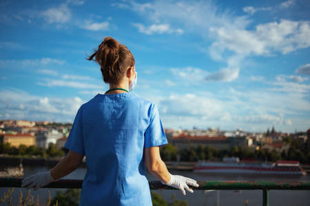 covid-19 pandemic. tired modern physician woman in scrubs with stethoscope, medical mask and rubber gloves outside near wall.の写真素材