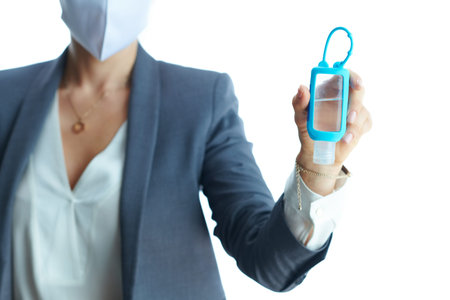 Business during covid-19 pandemic. Closeup on female in a grey suit with medical mask showing sanitiser isolated on white background.の写真素材