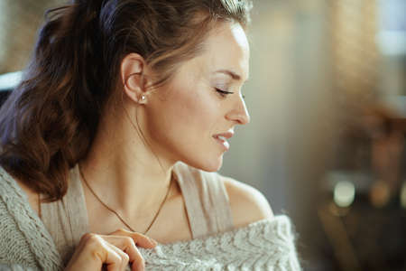 pensive young female in knitted cosy cardigan with book in the modern living room in sunny autumn day.の写真素材
