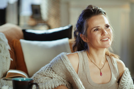 pensive young female in knitted cosy cardigan with book in the modern living room in sunny autumn day.の写真素材