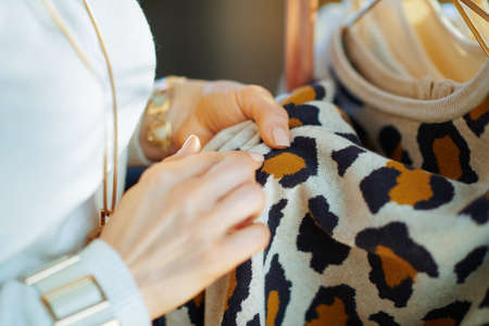 Closeup on trendy middle age housewife in white sweater and skirt with pile of sweaters and cup of tea with lemon at modern home in sunny winter day.の写真素材