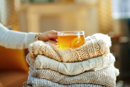 Closeup on trendy middle age housewife in white sweater and skirt with pile of sweaters and cup of...