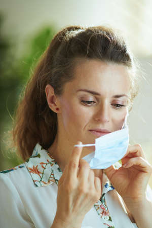 Life during covid-19 pandemic. Portrait of elegant female in white blouse wearing medical mask.の写真素材