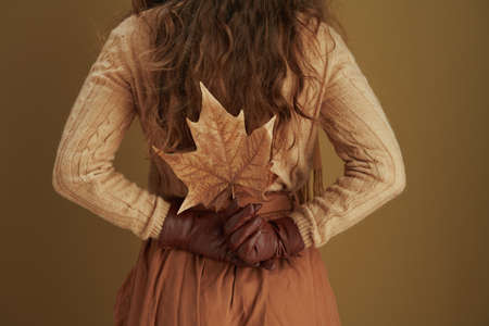 Life during coronavirus pandemic. cheerful elegant 40 years old housewife in scarf with white medical mask and yellow autumn maple leaves against beige background.の写真素材