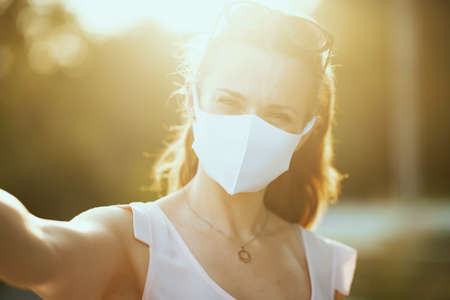 pensive modern woman in pink blouse with white mask and sunglasses looking into the distance outdoors in the city.の写真素材