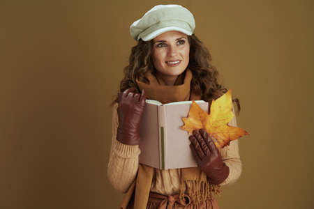 Hello october. smiling stylish 40 years old woman in scarf with leather gloves and paper shopping bag against beige background.の写真素材