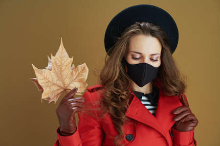 Hello autumn. young housewife in red coat with black mask, cup and paper shopping bags isolated on bronze background.の写真素材