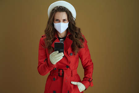 Life during coronavirus pandemic. Closeup on female in red coat sending text message using smartphone on bronze background.の写真素材