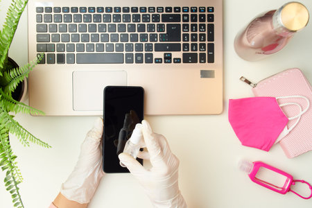 Upper view of female hands in white rubber gloves using laptop near medical mask, an antibacterial...