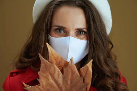 Hello autumn. Portrait of happy modern middle aged woman in red coat showing smartphone blank screen against beige background.の写真素材