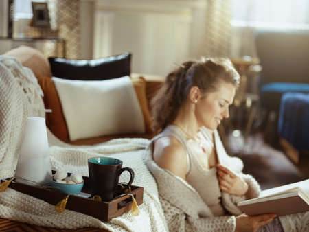 happy young woman in knitted cosy cardigan with book in the modern living room in sunny autumn day.の写真素材