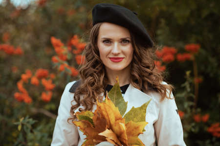 Hello october. Portrait of smiling stylish female in beige trench coat outside on the city street in autumn.の写真素材