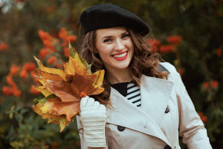 Hello october. Portrait of smiling stylish female in beige trench coat outside on the city street in autumn.の写真素材