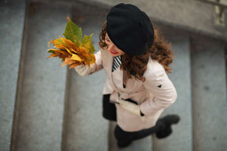 Hello october. Portrait of smiling stylish female in beige trench coat outside on the city street in autumn.の写真素材